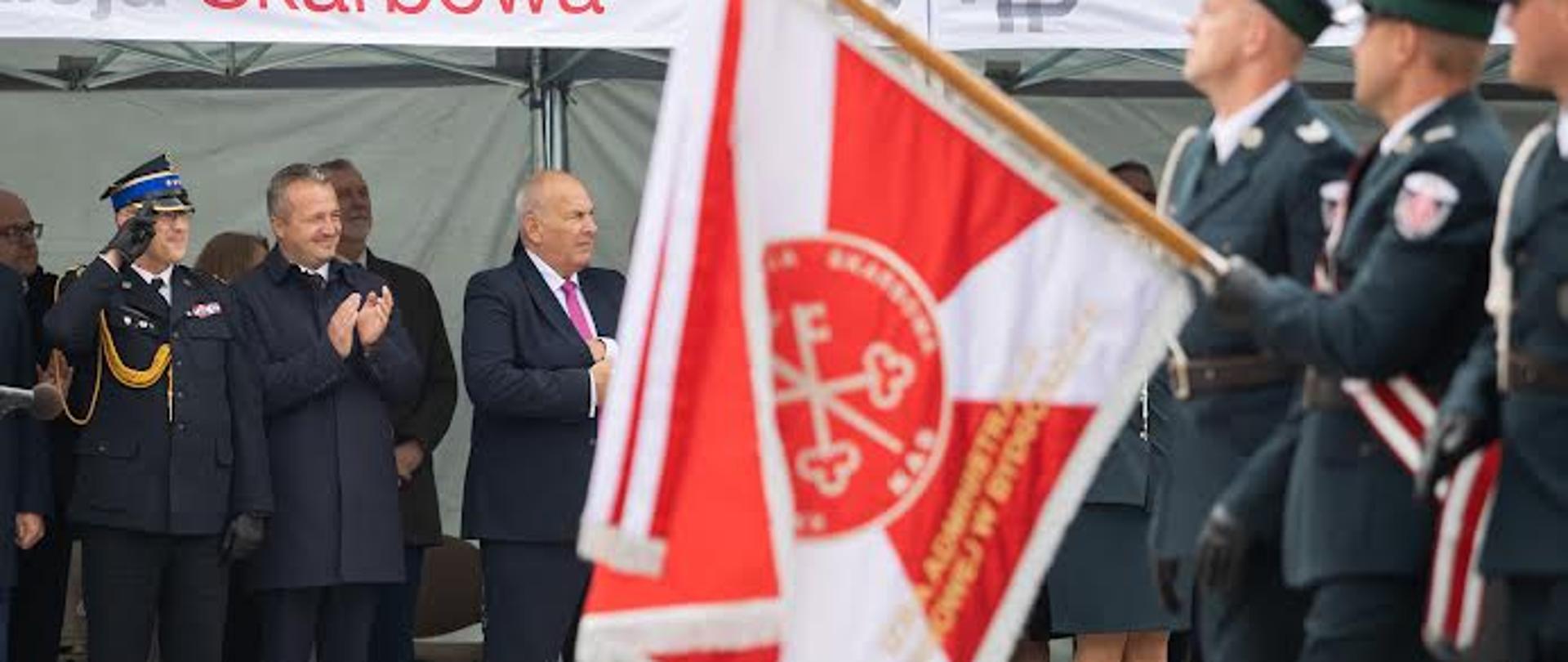 Na pierwszym planie sztandar Krajowej Administracji Skarbowej, w tle stoi wojewoda kujawsko-pomorski pan Mikołaj Bogdanowicz, po jego prawej stronie kujawsko-pomorski Komendant Wojewódzki PSP st. bryg. Jacek Kaczmarek