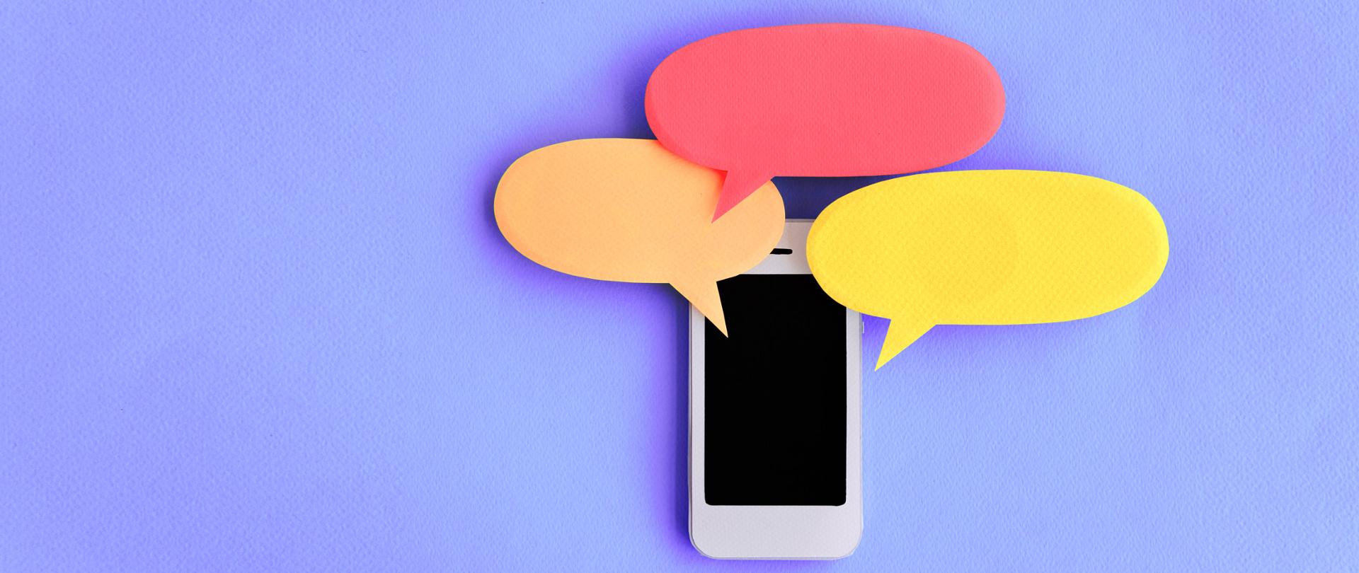 Biały smartfon na fioletowym tle - wokół niego trzy karteczki (żółta, pomarańczowa i czerwona) w kształcie chmurek dialogowych.