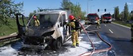 Zdjęcie przedstawia ugaszony pożar samochodu dostawczego. Na zdjęciu widać strażaków, którzy dogaszają pożar. Ponadto na zdjęciu widać samochody strażackie. 