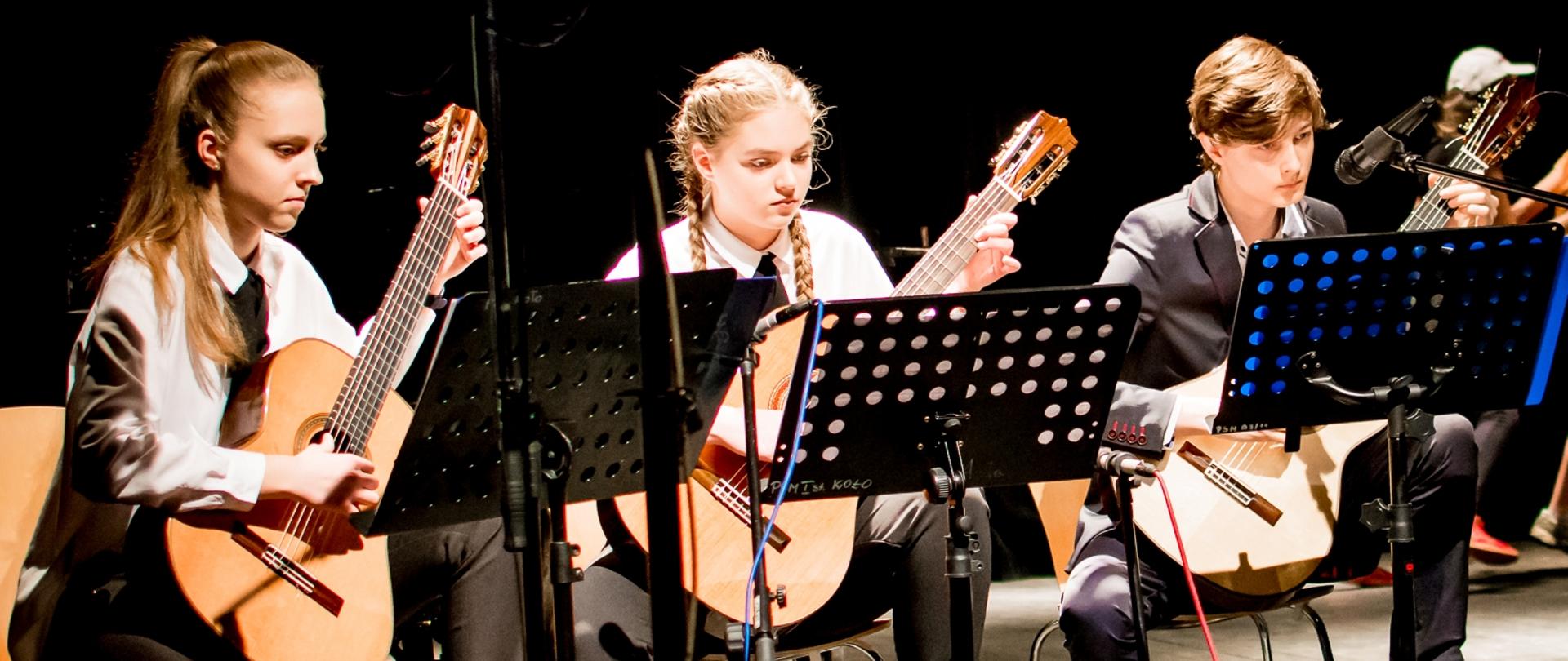 Uczniowie z zespołu gitarowego grający na gitarach podczas koncertu