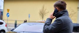 Mężczyzna w płaszczu rozmawia przez telefon, w tle stoi zapakowany samochód 