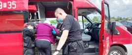 Na zdjęciu druhowie pomagający wsiąść do pojazdu seniorce