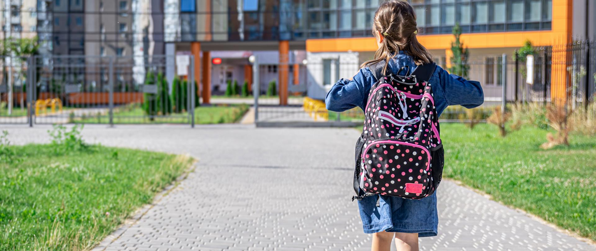 Zdjęcie przedstawia dziewczynkę z plecakiem, która maszeruje do szkoły.