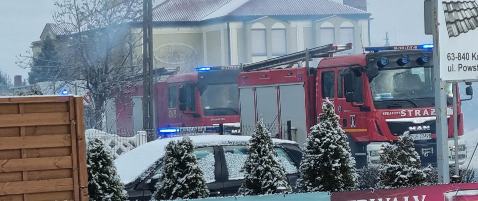 Zdjęcie przedstawia samochody strażackie stojące na drodze podczas działań związanych z pożarem sadzy w kominie.