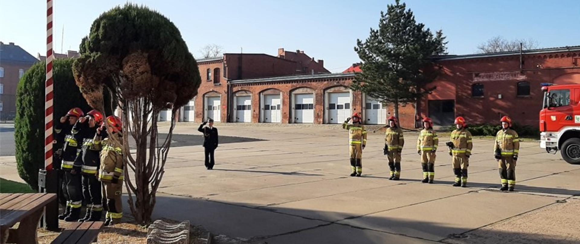Zdjęcie przedstawia strażaków oddających honor podczas uroczystego podnoszenia flagi ma maszt
