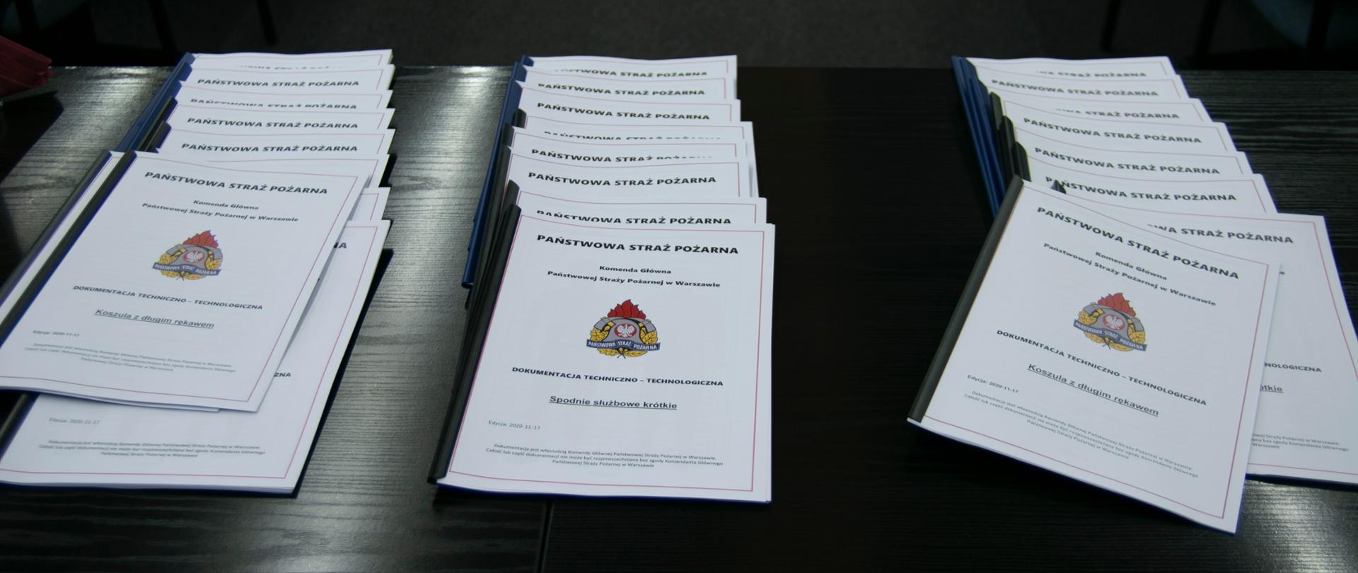 na stole leżą trzy kolumny dokumentacji technicznej nowego wzoru umundurowania