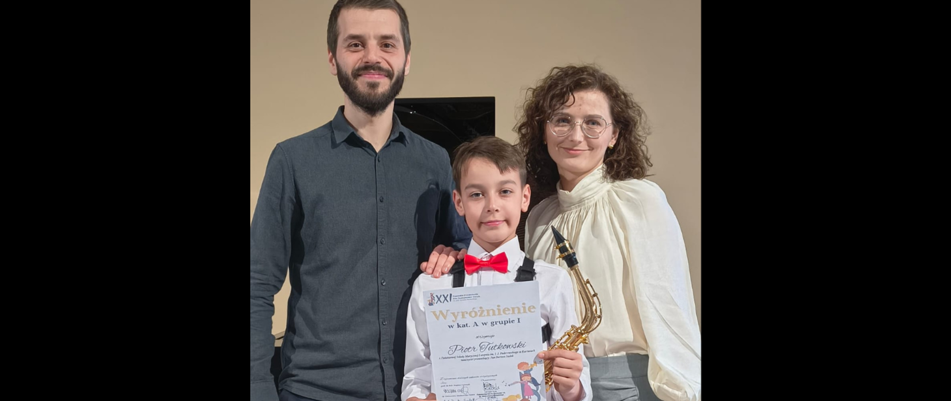 uczeń trzymający dyplom i saksofon w obecności nauczycieli