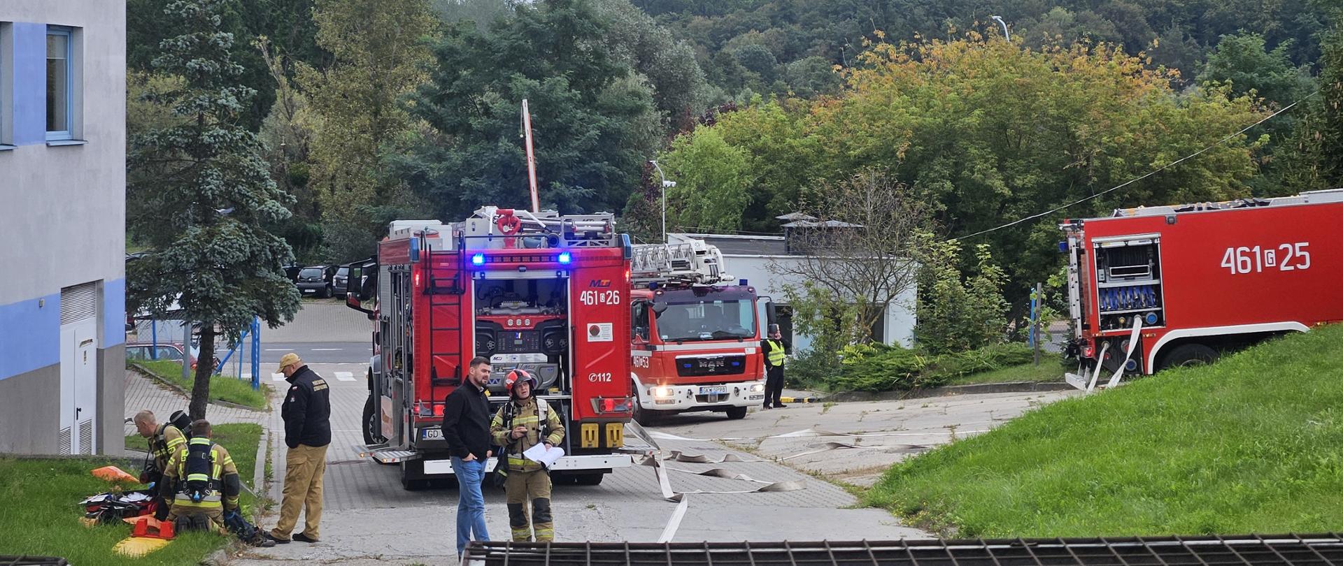 Strażacy i pojazdy podczas ćwiczeń przed budynkami FPK
