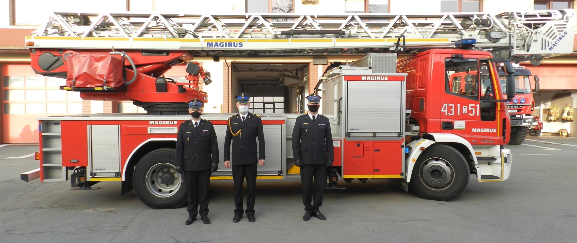 Strażacy PSP w umundurowaniu wyjściowym na tle drabiny mechanicznej 