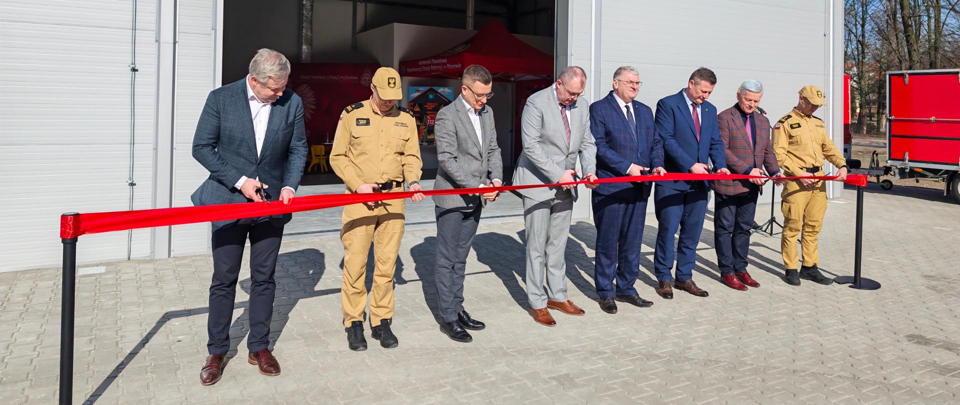 grupa osób przecinający wstęgę przed nowo otwieranym magazynem