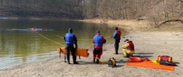 Na zdjęciu widzimy strażaków podczas ewakuacji poszkodowanego z jeziora oraz strażaków na brzegu, którzy ich zabezpieczają