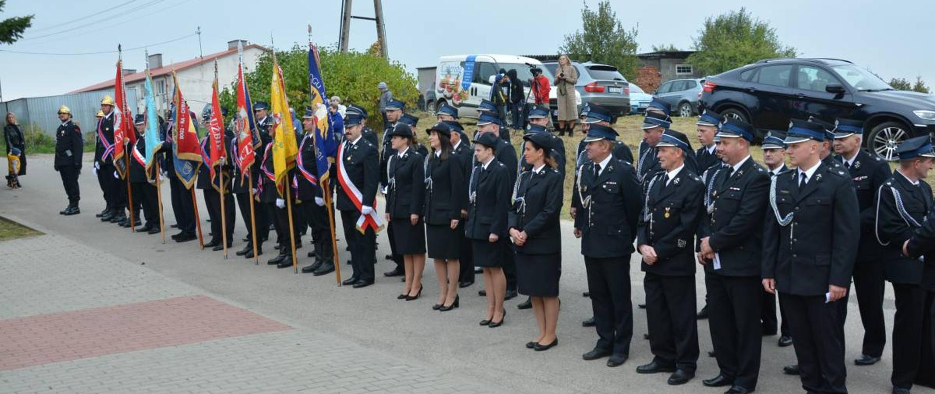 Ustawione w szeregu poczty sztandarowe i strażacy biorący udział w uroczystości.