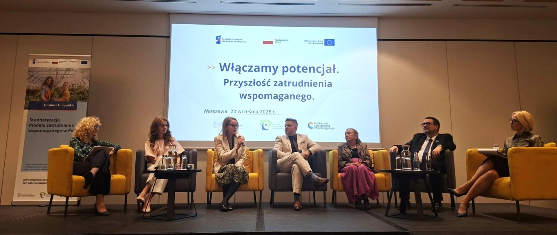 Paneliści siedzą na fotelach, odpowiadają na pytania 