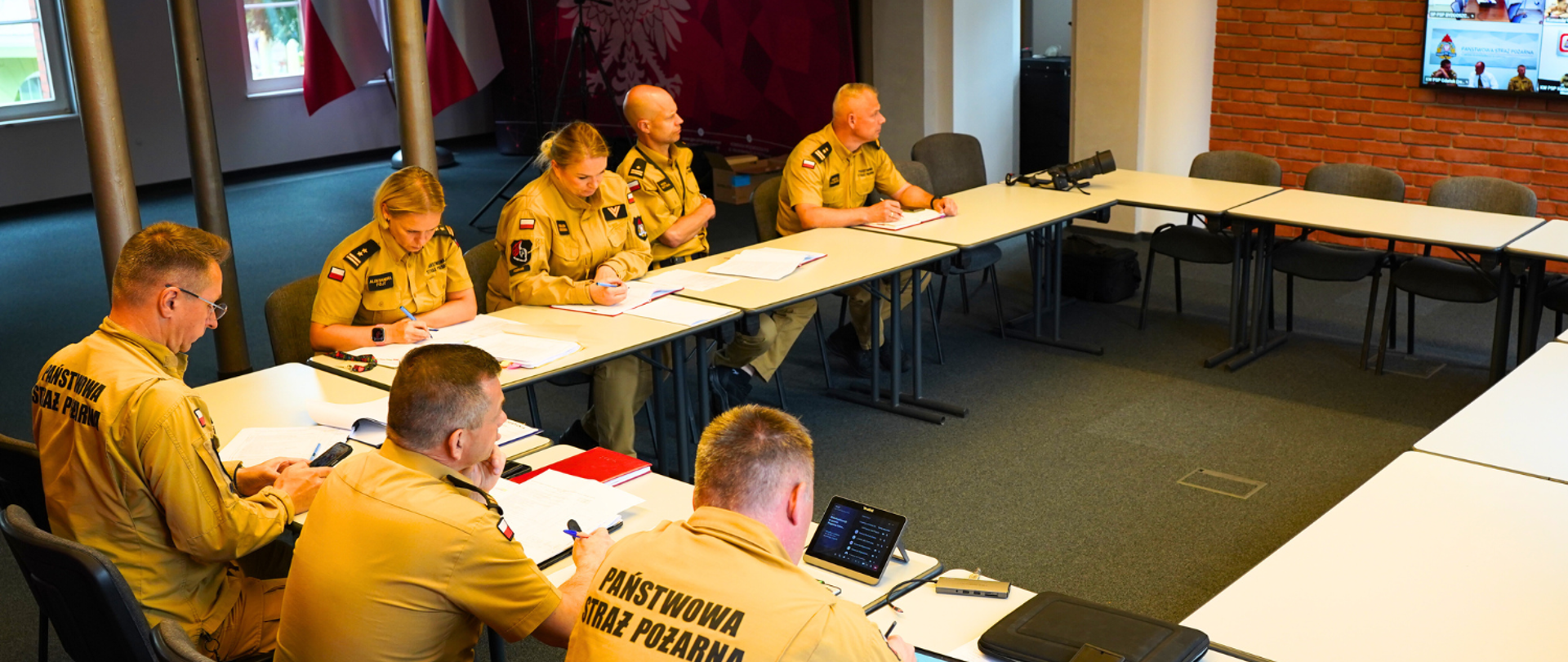 Panowie Komendanci oraz naczelnicy wydziałów zajęli miejsca za stołem, na sali, przed telewizorem, gdzie odbywa się wideokonferencja.
