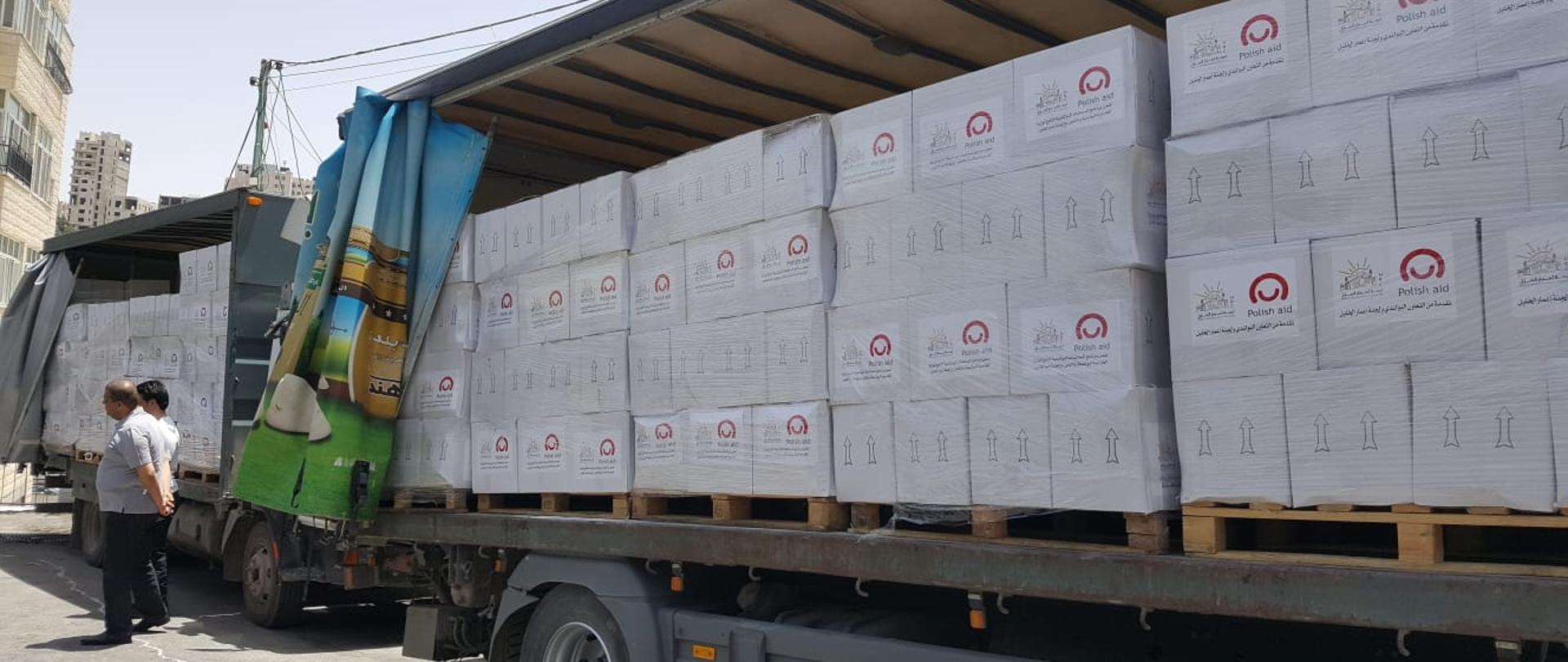 Samochód tir z białymi paczkami z żywnością z logo Polska pomoc i innymi znakami