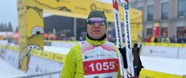 Zdjęcie przedstawia asp. Jarosława Gacek n tle baneru startowego. Ubiór zimowy, w dłoni trzyma narty