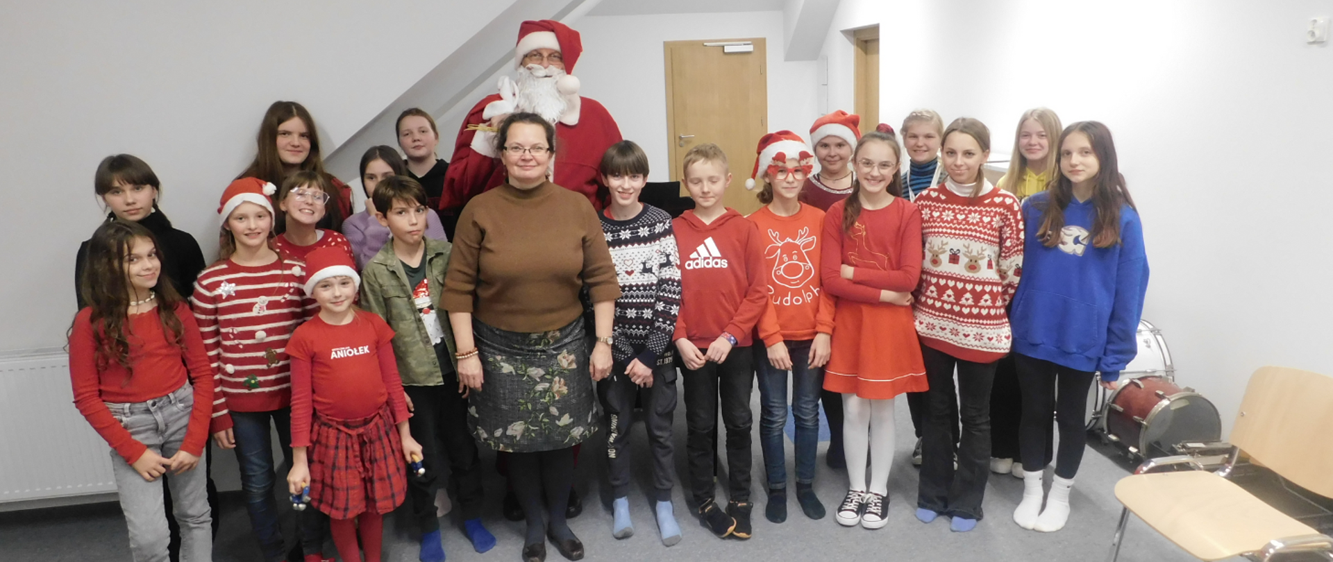 Na zdjęciu duża grupa uczniów ze Świętym Mikołajem. Na strojach dzieci dominuje kolor czerwony. Część z nich ma założone czapeczki mikołajkowe.