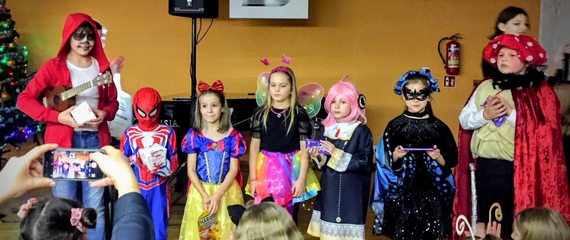 Impreza choinkowa. Konkurs na najlepszy strój. Laureaci. Uczniowie pozują do zdjęć. Kolorowo. Scena koncertowa.