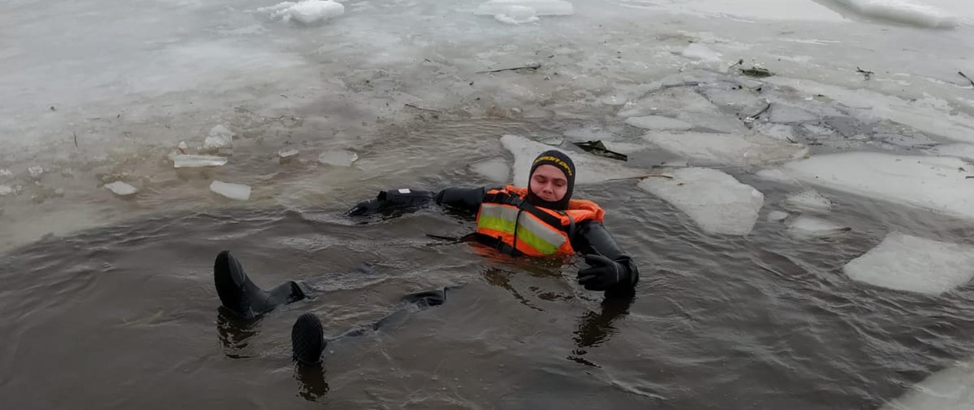 Funkcjonariusz z JRG Stargard w ubraniu suchym i kamizelce wypornościowej pływa w przerębli.