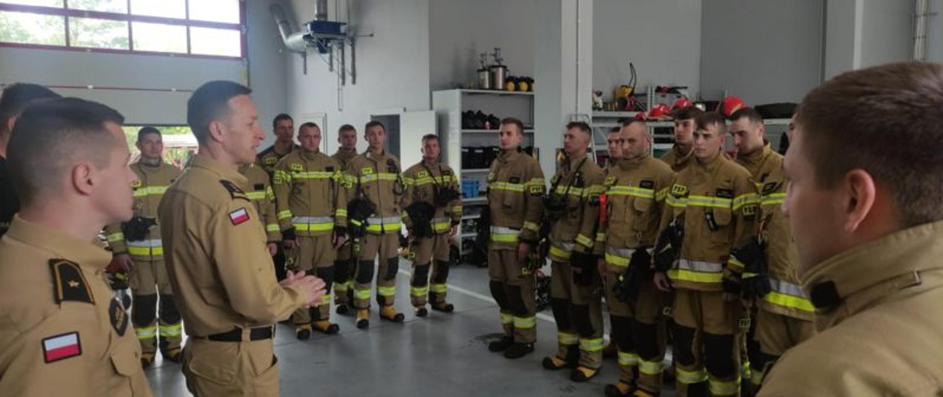 strażak przemawia do grupy strażaków stojących w garażu w mundurach specjalnych