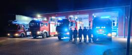plac przed komendą powiatową psp w brzezinach cztery samochody bojowe stoją przed garażami z włączonymi światłami alarmowymi niebieskimi przed samochodami strażacy na baczność skłądają hołd zmarłemu funkcjonariuszowi .