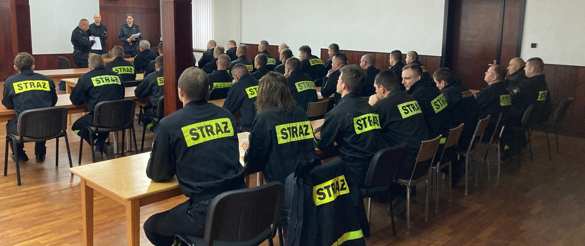 Strażacy siedzą na sali szkoleniowej podczas egzaminu z kwalifikowanej pierwszej pomocy.