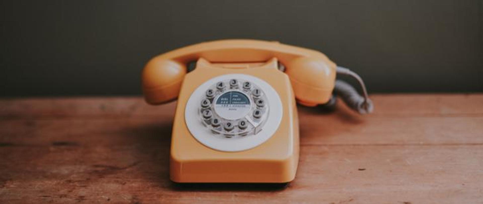 Zdjęcie telefonu starego typu w kolorze żółtym na drewnianym blacie.