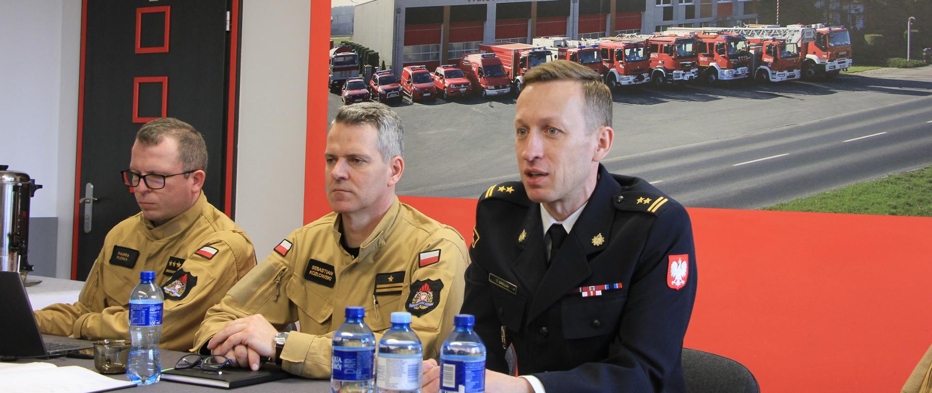 Trzech strażaków w mundurach siedzi przy stole.
