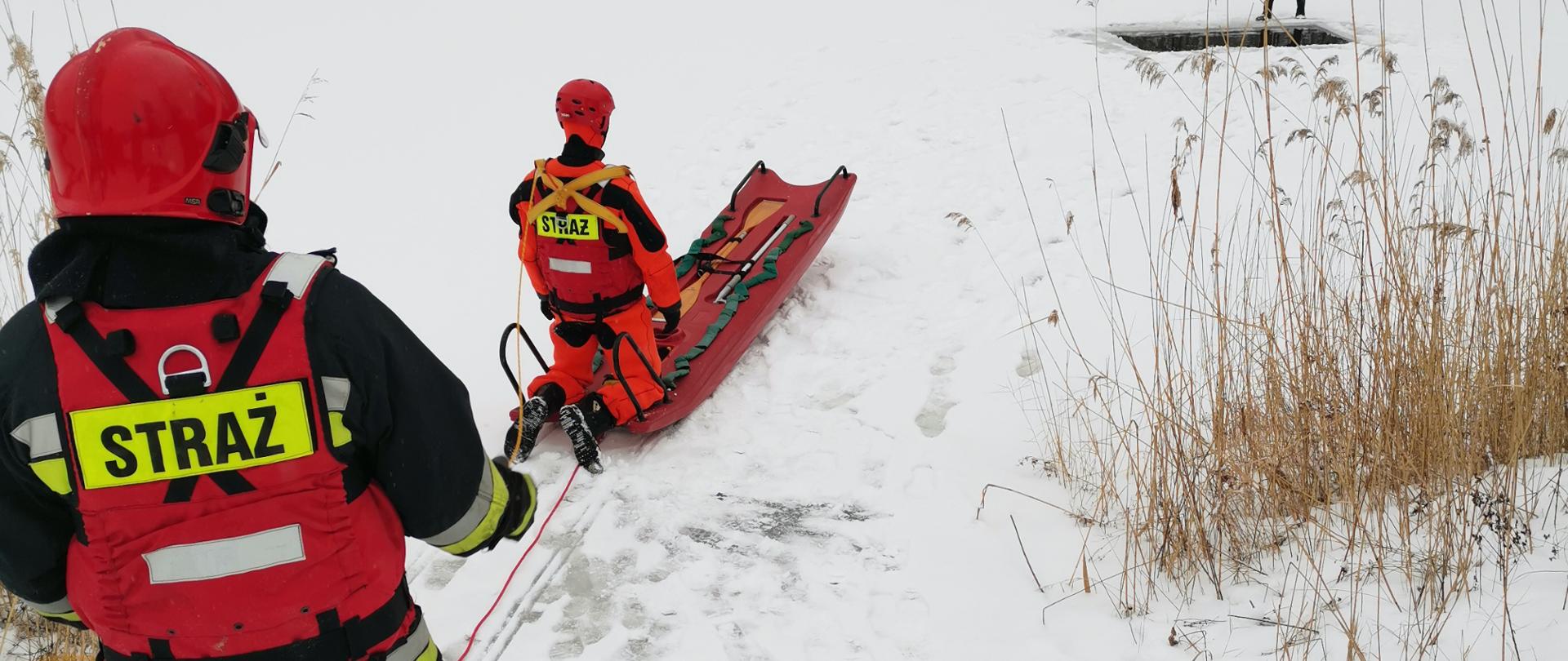 na zdjeciu widać strażaków w kombinezonach ćwiczących podejmowanie osób poszkodowanyh na lodzie