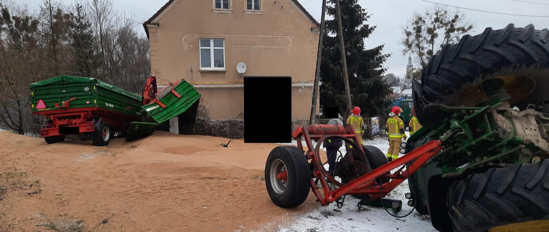 Widać przyczepę rolniczą blisko budynku, rozsypane zboże na poboczu, oś przyczepy oraz koła ciągnika