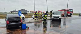Dwa uszkodzone samochody, w pobliżu strażacy, za nimi samochód straży