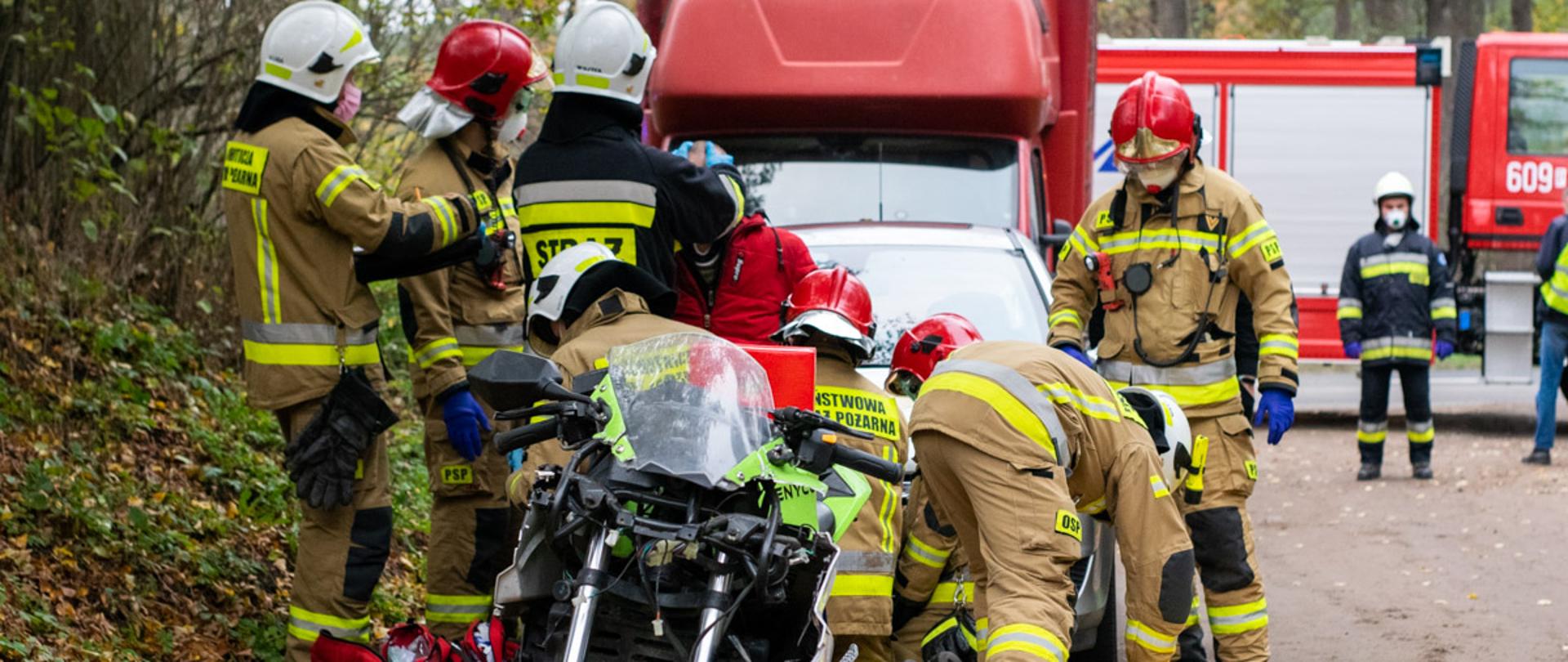 Na zdjęciu ratownicy udzielający pomocy poszkodowanemu motocykliście, w tle samochód dostawczy i ratowniczo gaśniczy