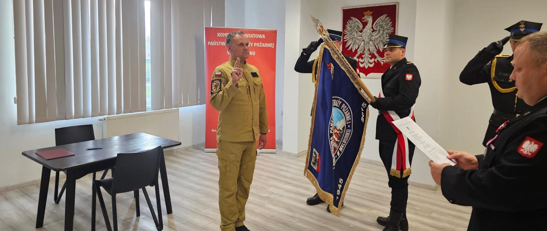 Strażak stoi przy sztandarze podczas ślubowania na sali sztandarowej