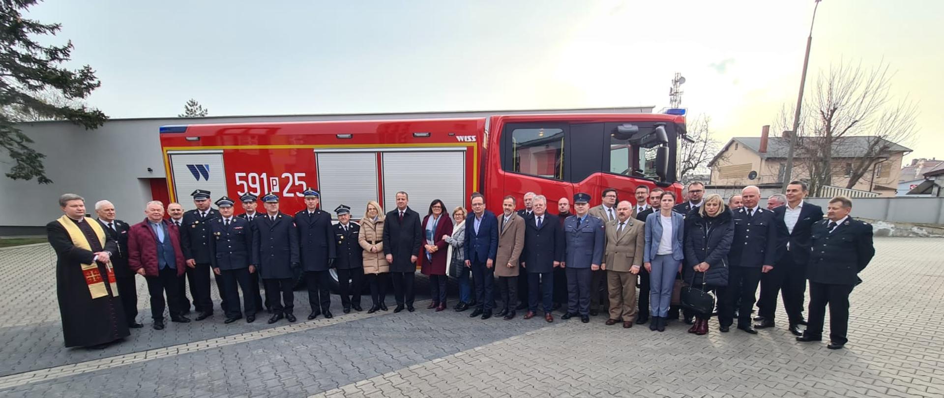Widać funkcjonariuszy, zaproszonych gości, strażaków na zdjęciu grupowym na tle nowego samochodu
