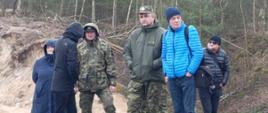 Wizja terenowa na odcinku przygranicznym z Białorusią. Przedstawiciele służb podczas wizji terenowej. Grupa kilku osób stoi na brzegu rzeki.