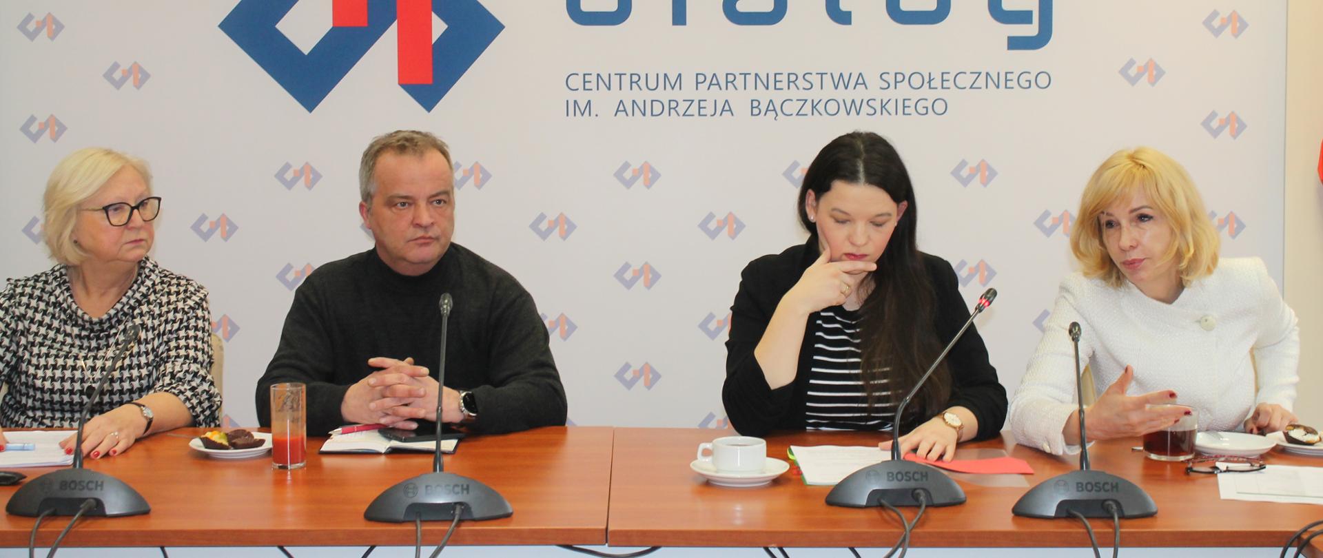 Na zdjęciu widnieje stół prezydialny za którym siedzi wiceminister Rodziny, Pracy i Polityki społecznej – Katarzyna Nowakowska, która prowadzi spotkanie. W tle znajduje się baner z napisem Centrum Partnerstwa Społecznego Dialog. Po lewej stronie Ministry siedzi Urszula Demkow- Podsekretarz Stanu w Ministerstwie Zdrowia a po prawej stronie zasiadają współprzewodnicząca Zespołu ze strony pracodawców – Teresa Hernik oraz Zbigniew Spendel – współprzewodniczący strony związkowej. 