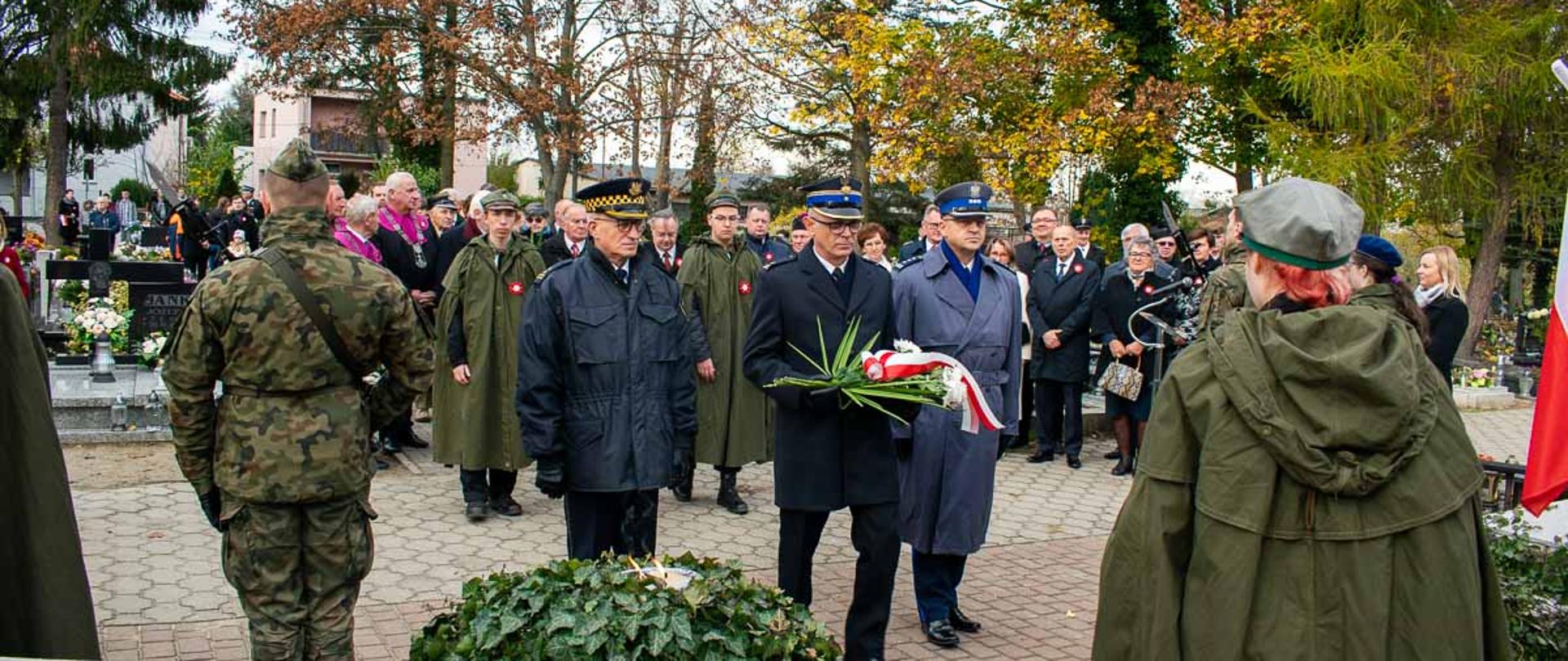 Zdjęcie wykonane na cmentarzu parafialnym podczas składania wiązanki kwiatów przez Komendanta PSP w Śremie. Uczestnikami obchodów widocznymi na zdjęciu są m.in. Żołnierze oraz harcerze. 