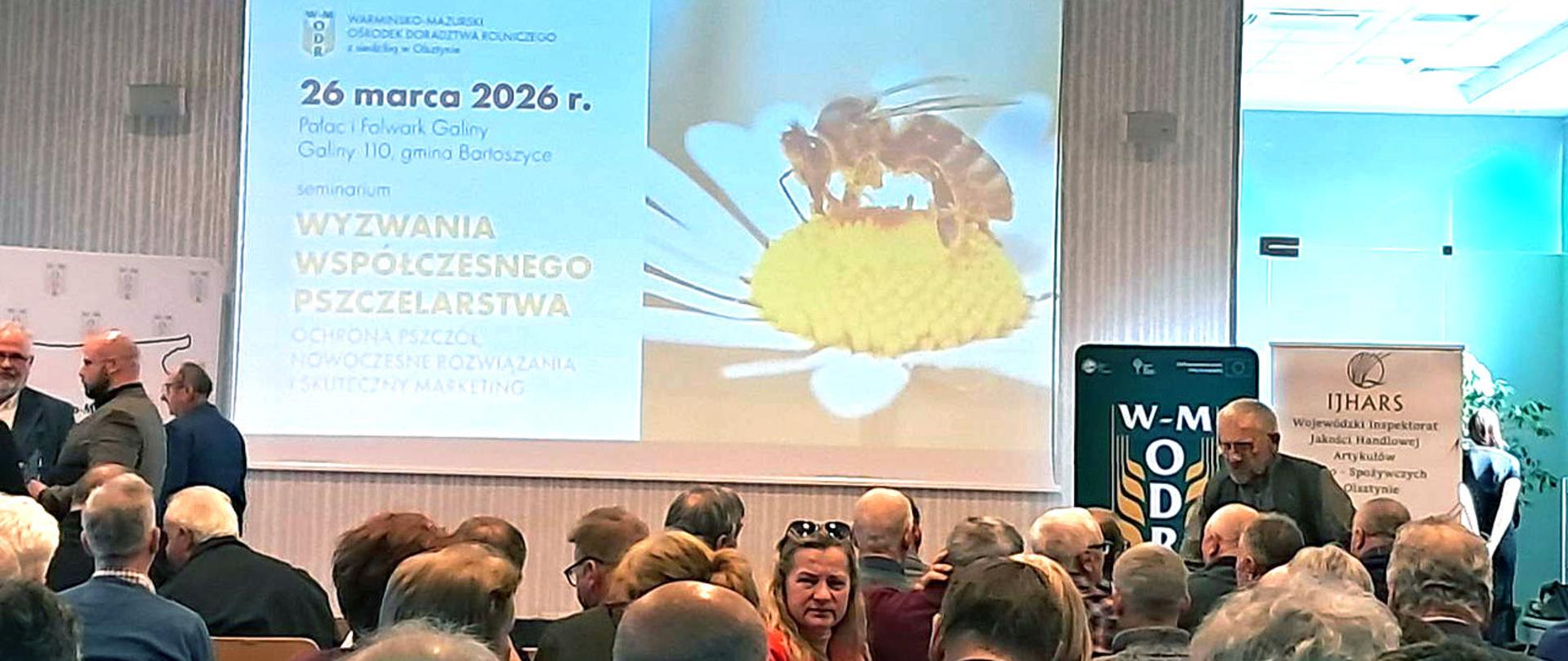 na pierwszym planie wyświetlony slajd z tematem seminarium "Wyzwania współczesnego pszczelarstwa"