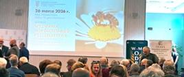 na pierwszym planie wyświetlony slajd z tematem seminarium "Wyzwania współczesnego pszczelarstwa", przed nim siedzą uczestnicy