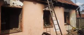 Pożar budynku mieszkalnego. Widok z podwórza na budynek, w którym powstał pożar. Widoczne są ślady opaleń elewacji zewnętrznej oraz stolarki okiennej. O dach budynku oparta jest drewniana drabina.