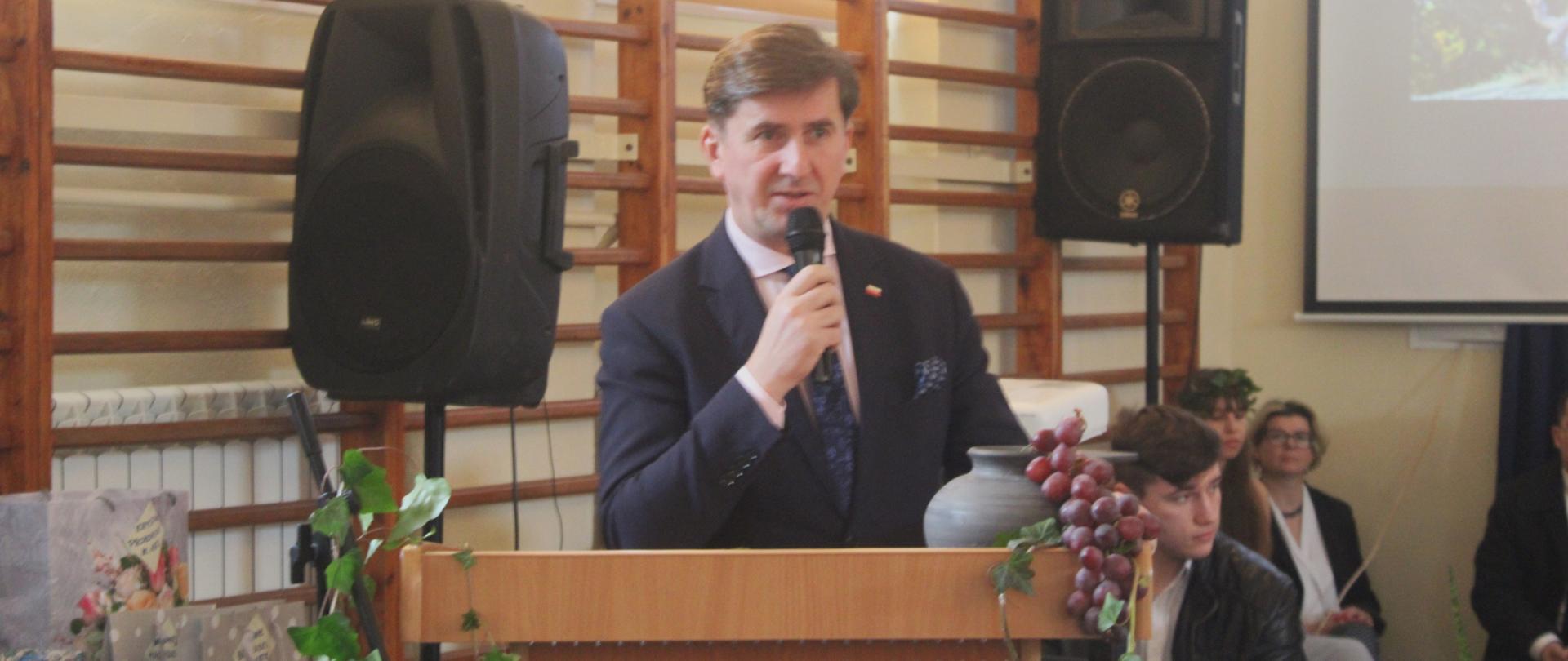 Sekretarz stanu Rafał Romanowski stojący przy mównicy z mikrofonem w dłoni