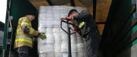 Strażacy KP PSP w Wadowicach wraz z kierowcą ustawiają na skrzyni ładunkowej ciężarówki palety z artykułami higienicznymi. 