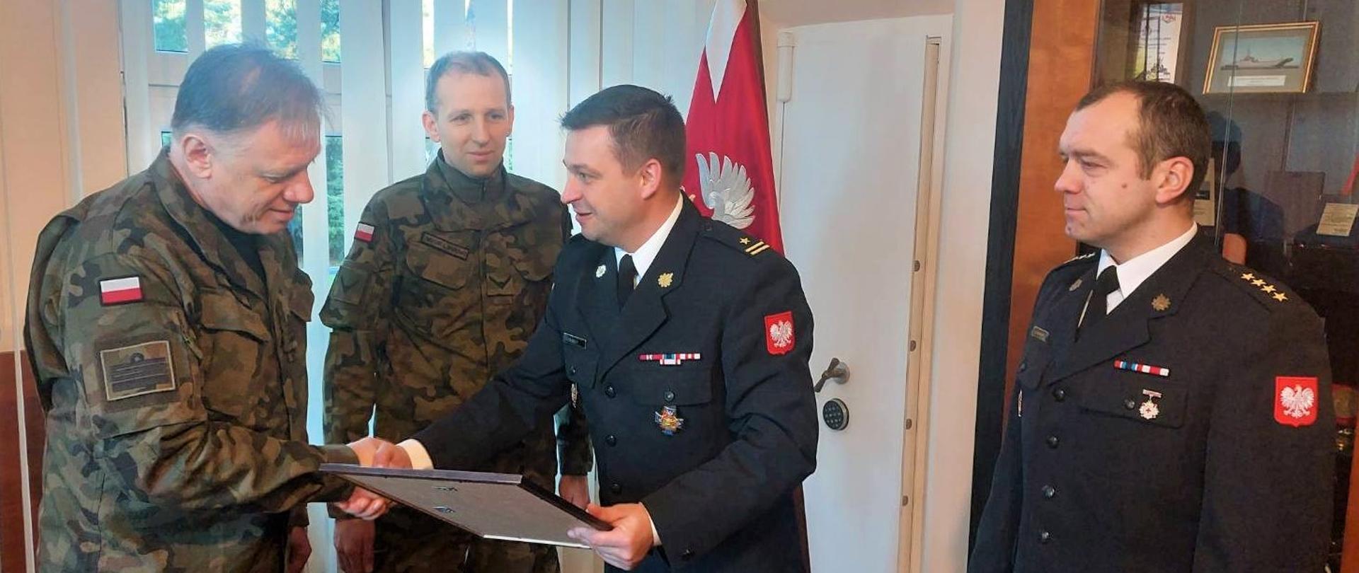 Zdjęcie przedstawia symbolicznie przekazano na ręce kmdr-a Grzegorza Okuljara, Komendanta Centrum Szkolenia Marynarki Wojennej w Ustce decyzję o ponownym włączeniu na kolejne 5 lat do krajowego systemu ratowniczo-gaśniczego Wojskowej Straży Pożarnej CSMW w Ustce. 