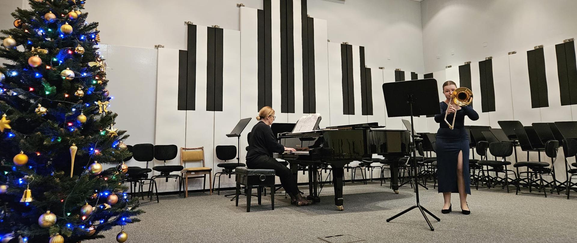 Nastolatka gra na puzonie, obok kobieta gra na fortepianie.