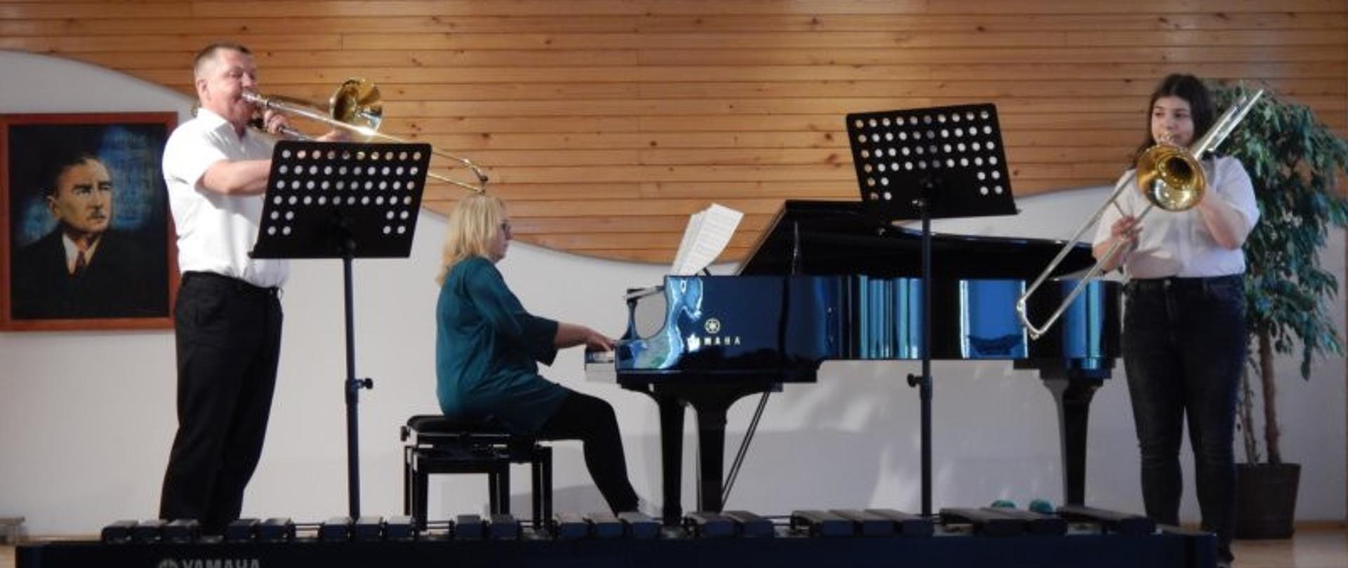 Trzy osoby grające na scenie , dwie osoby na puzonach i jedna osoba na fortepianie