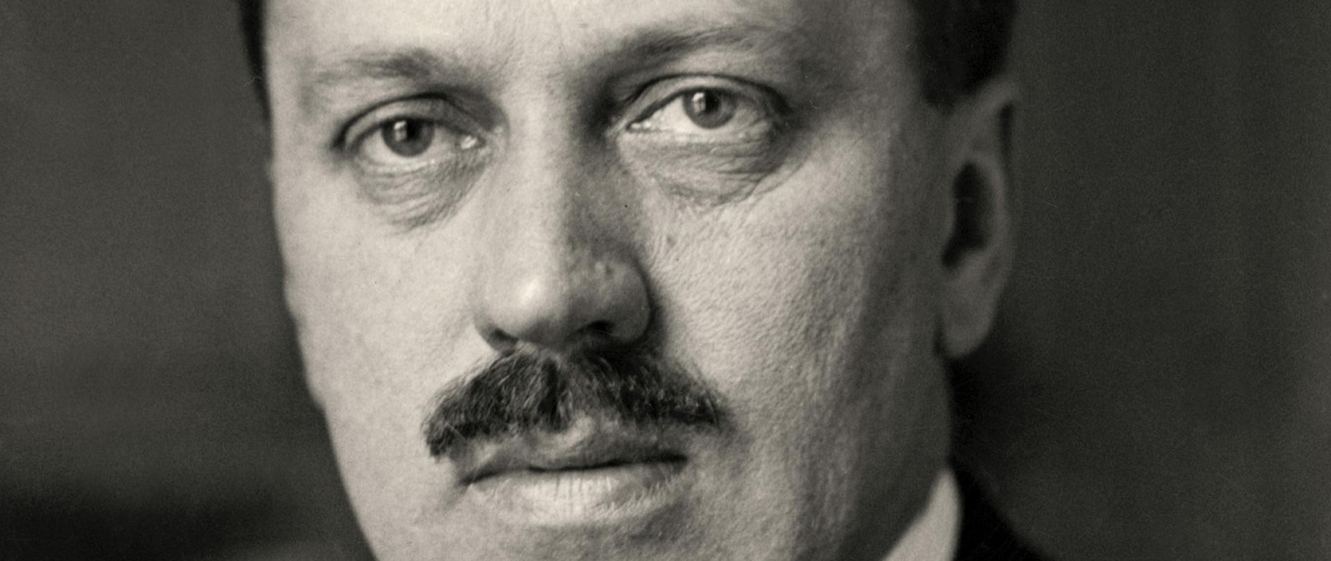 Aleksander Skrzyński - premier i minister spraw zagranicznych czarno-biały portret mężczyzny z wąsem, ciemnymi włosami, jasny krawat, ciemna marynarka biała koszula w drobne ciemne paski.