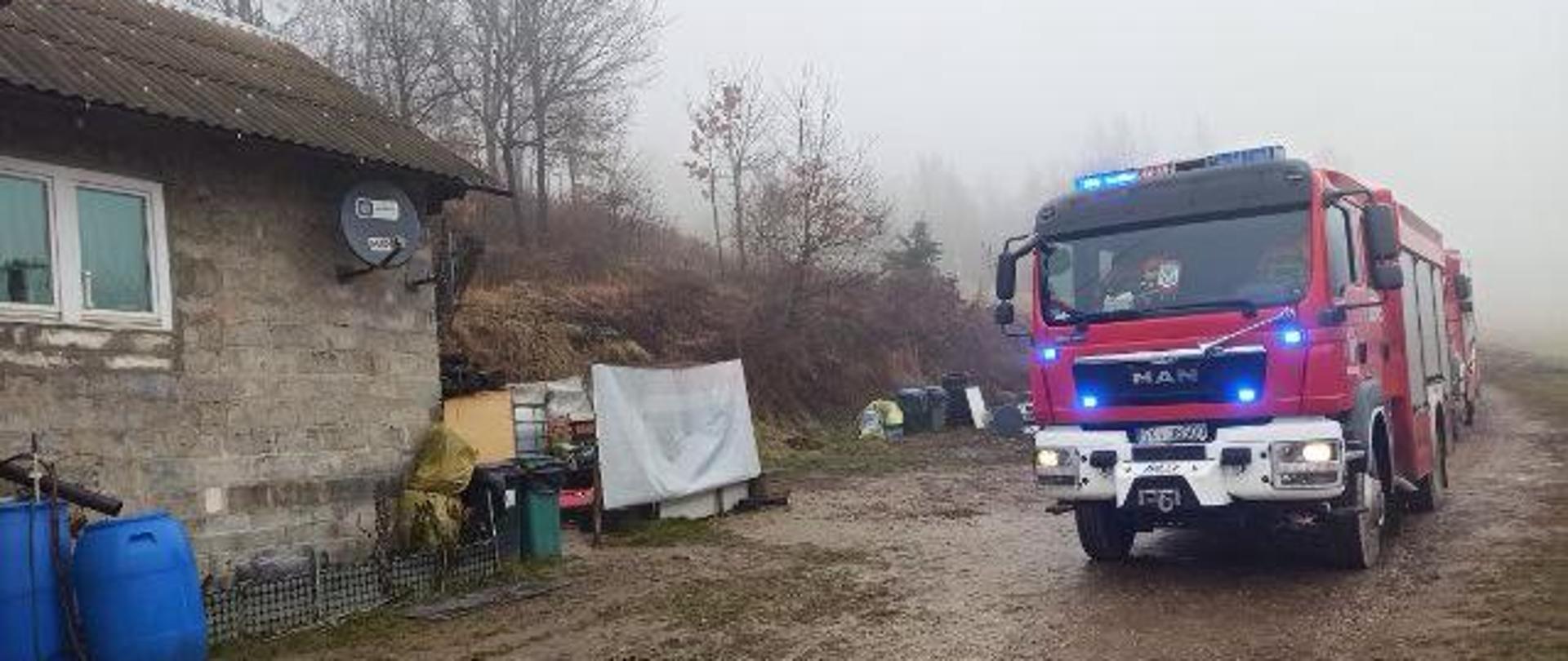 Zdjęcie przedstawia dom jednorodzinny (po lewej stronie) gdzie doszło do zdarzenia. Po prawej stronie widać samochody pożarnicze.