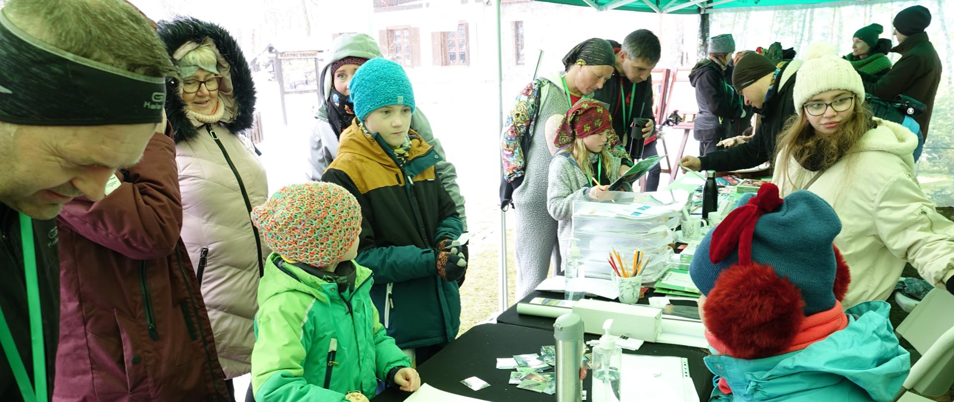 Widok na wnętrze namiotu, pośrodku stoły z pomocami edukacyjnymi, wokół prowadzący konkursy oraz uczestnicy