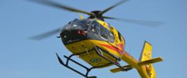 Na tle błękitnego nieba śmigłowiec ratunkowy. Maszyna podchodzi do lądowania.