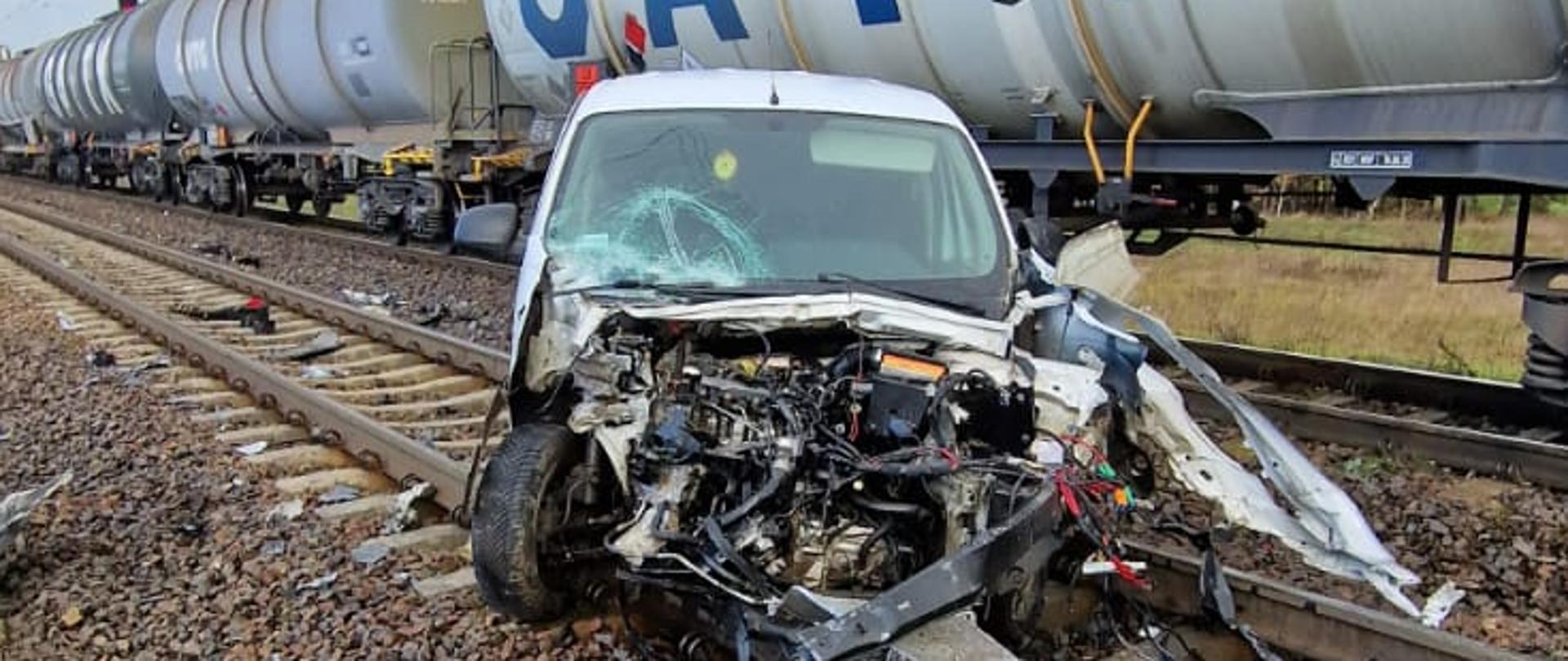 Zdjęcie przedstawia rozbity samochód osobowy oraz wagony pociągu towarowego